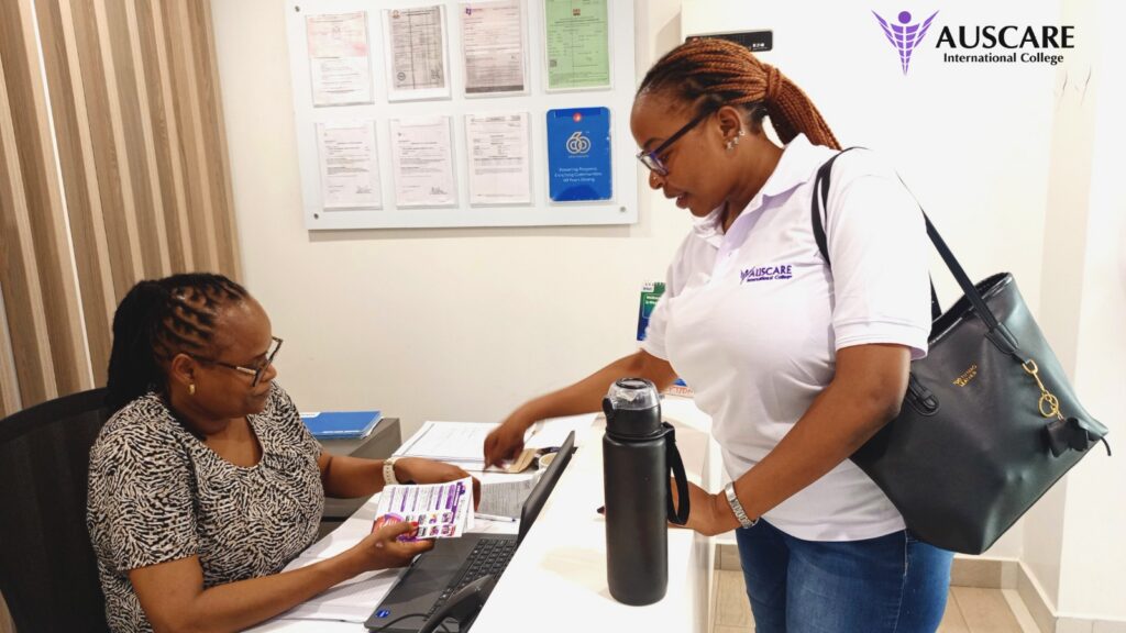 Reception scene: a staff member sits with a laptop while another woman hands her a brochure at AUSCARE International College