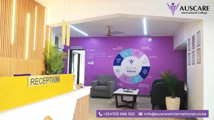 Reception desk with a bright yellow counter labeled RECEPTION and a purple wall featuring the Auscare Values graphic and seating area nearby.