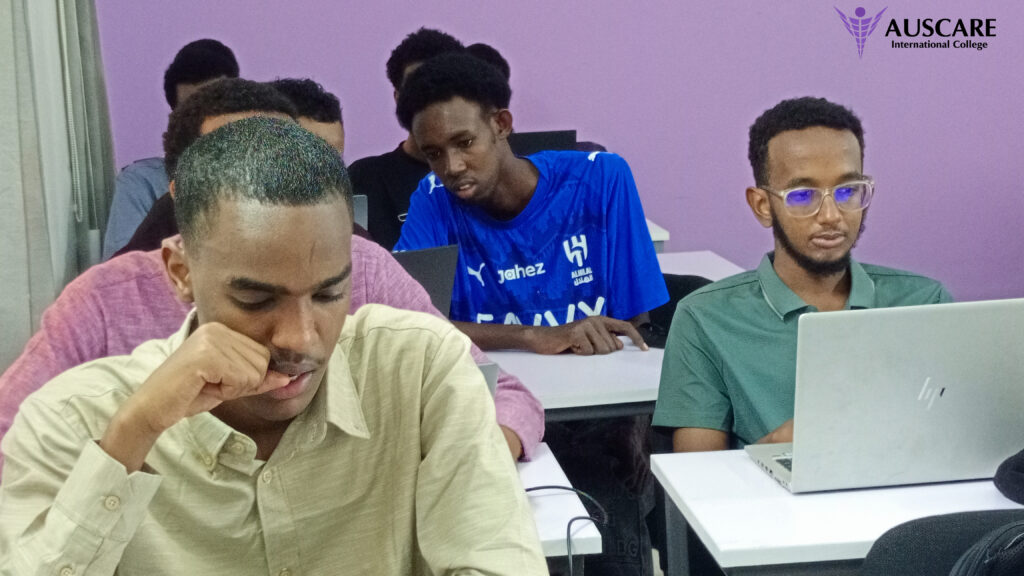 Group of students working at laptops in a classroom with a purple wall; AUSCARE International College logo in the corner. (informative)