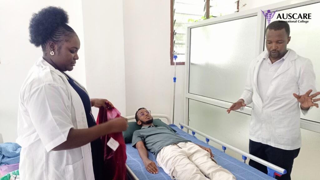 Nurse and doctor in white coats care for a man lying on a hospital bed in a clinical room; IV stand beside bed and AUSCARE logo top right.